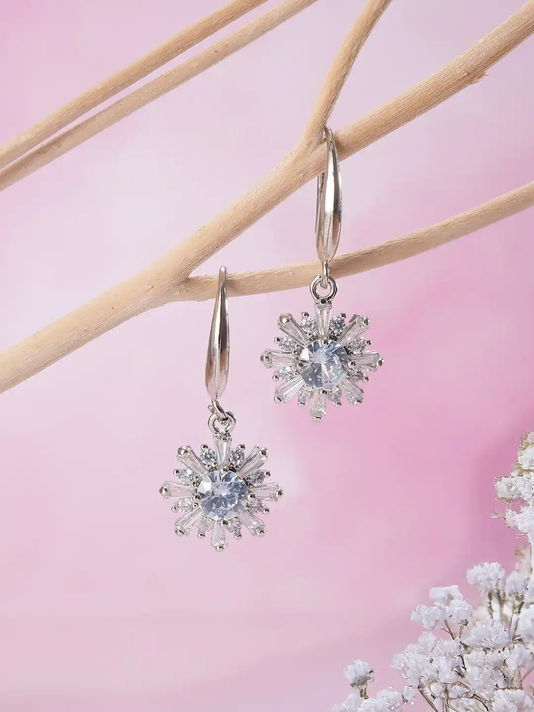 Silver snowflake earrings on a pink background with floral elements