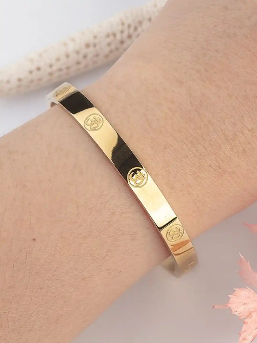 Gold bracelet with brand logo on a wrist against a neutral background